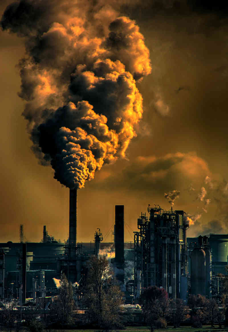 Industrial complex emitting from chimneys plumes of nicotine-coloured smoke into like-coloured sky